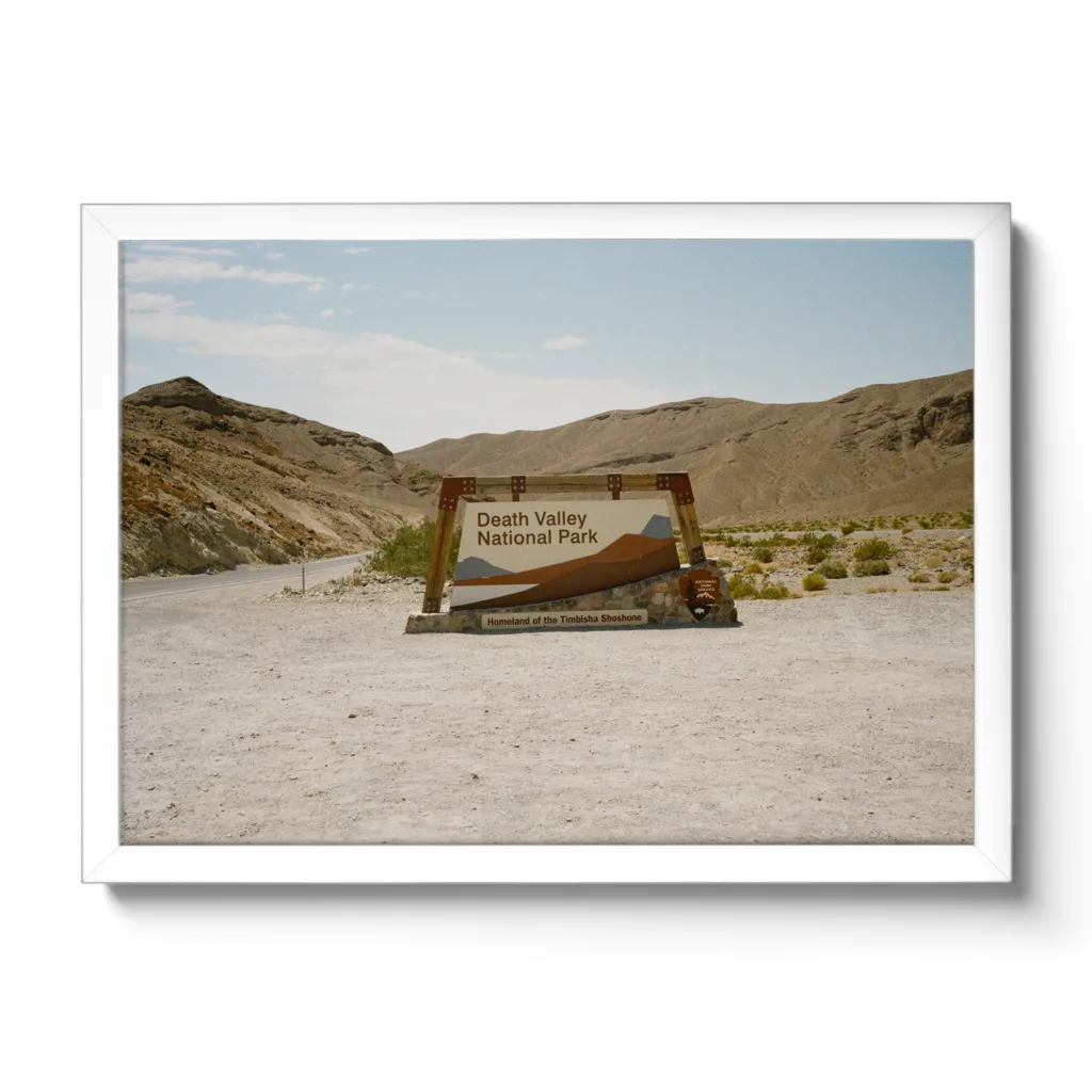 Bildaufnahme eines Schotterparkplatzes, mit dem Einfahrtsschild zum Death Valley National Park