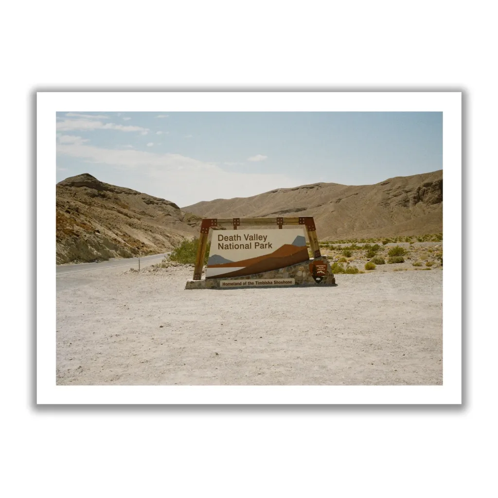 Bildaufnahme eines Schotterparkplatzes, mit dem Einfahrtsschild zum Death Valley National Park