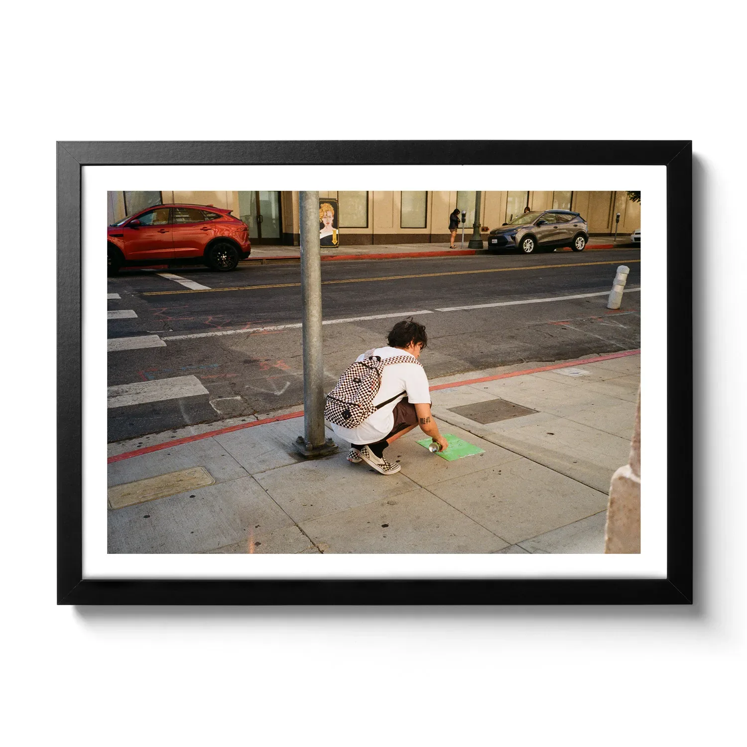 Image of a man spraying his tag with a spray can on the sidewalk.