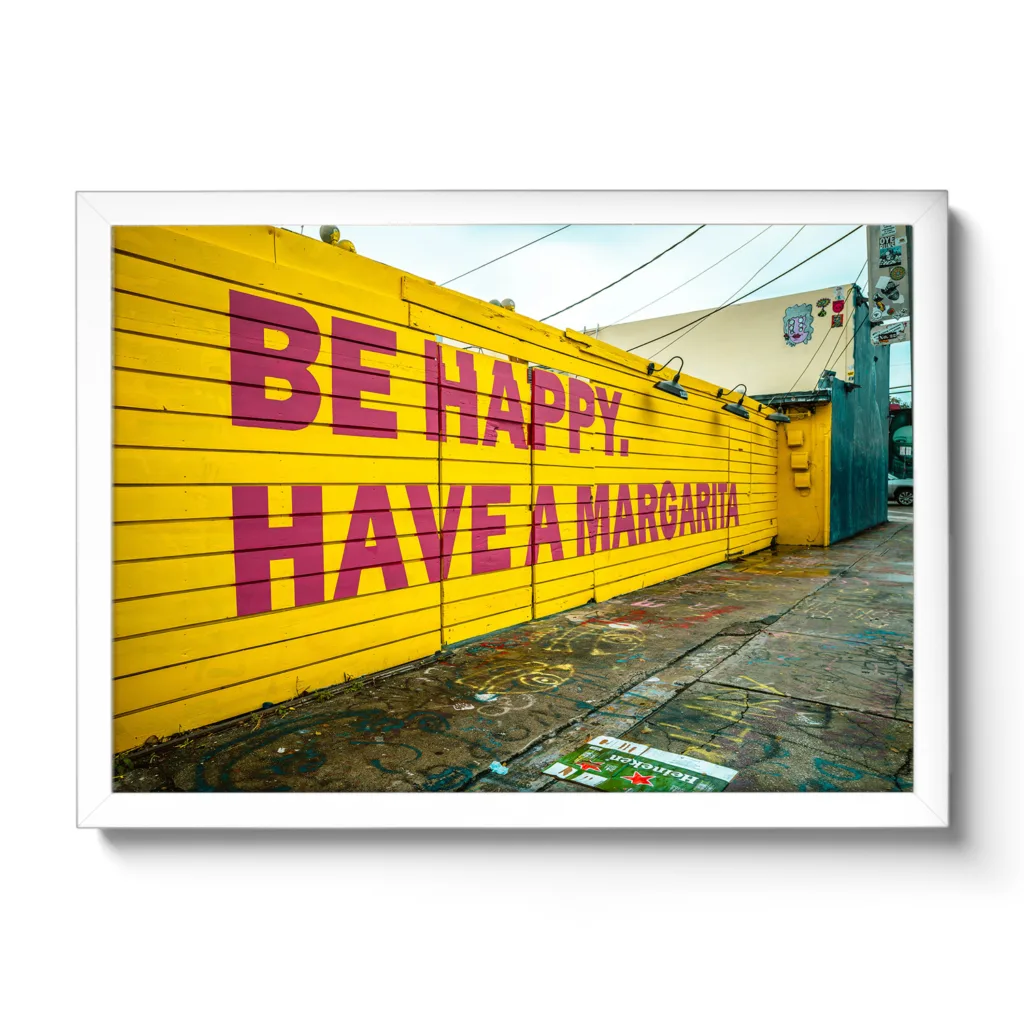 Bildaufnahme von einer gelben Wand mit dem Schriftzug "Be Happy Have a Margarita"