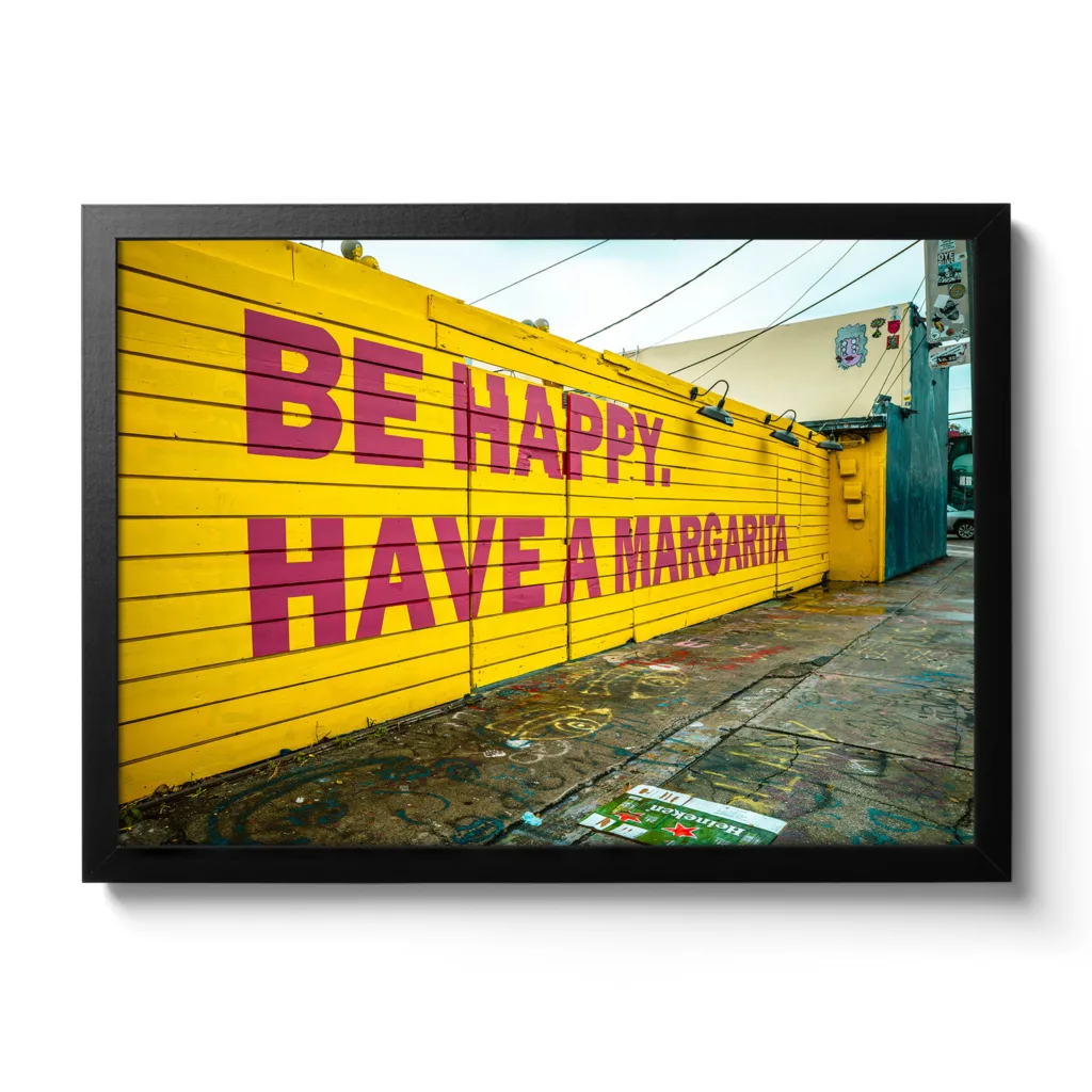 Bildaufnahme von einer gelben Wand mit dem Schriftzug "Be Happy Have a Margarita"