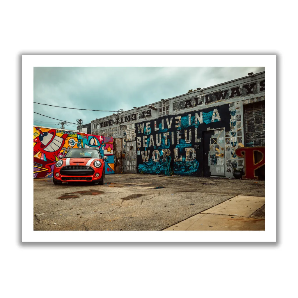 Bildaufnahme von einer Autowerkstatt, die mit Graffiti bemalt ist und ein roter Mini davor parkt.