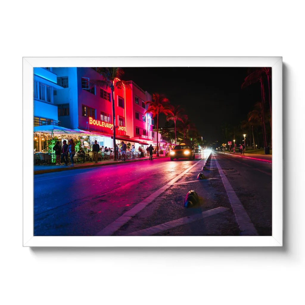 Bildaufnahme vom Ocean Drive in Miami bei Nacht. Neonlichter und ein fahrendes Auto.