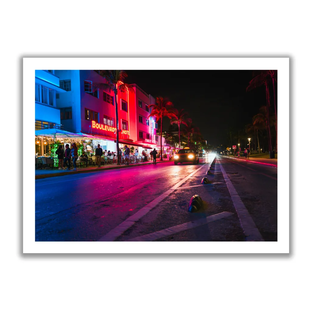 Bildaufnahme vom Ocean Drive in Miami bei Nacht. Neonlichter und ein fahrendes Auto.