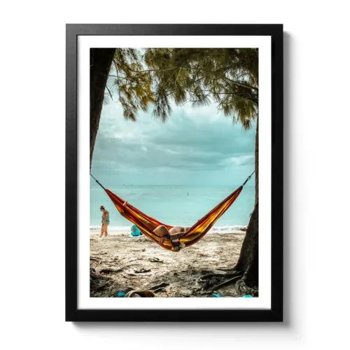 Picture of a man lying in a hammock on the beach under palm trees with the sea in the background. The funny thing is that you can see his little belly.