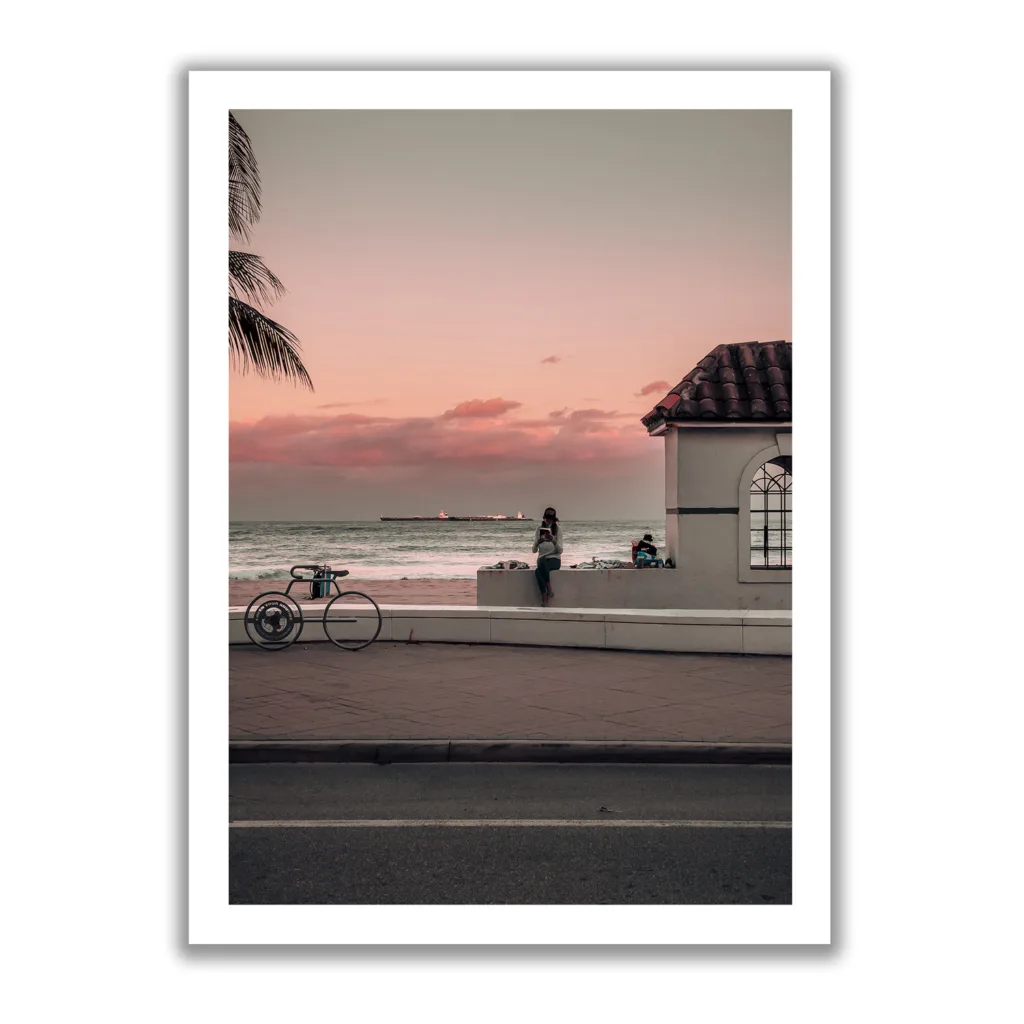 Bildaufnahme eines Sonnenuntergangs, wo eine Frau am Randstein sitzt und ein Buch liest. Im Hintergrund befindet sich das Meer und eine kleine weiße Hütte.