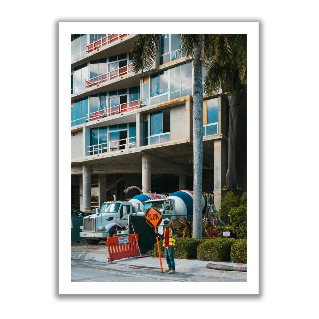 Baustellenbild mit einem jungen Mann, der ein Schild hochhält und Verkehrsteilnehmer warnt, langsam zu fahren.